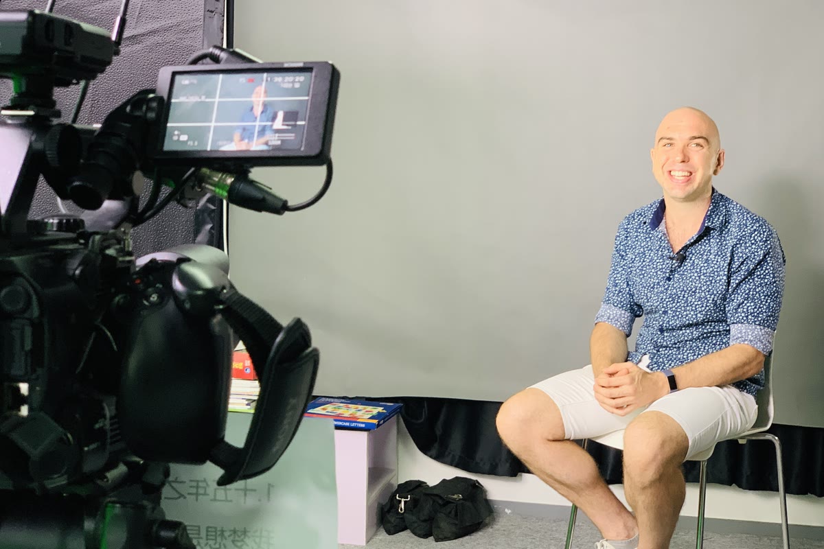James seated on a stool between two camera rigs, the crew’s monitor showing the take